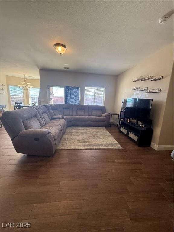 living area featuring dark wood-style floors, a textured ceiling, baseboards, and an inviting chandelier