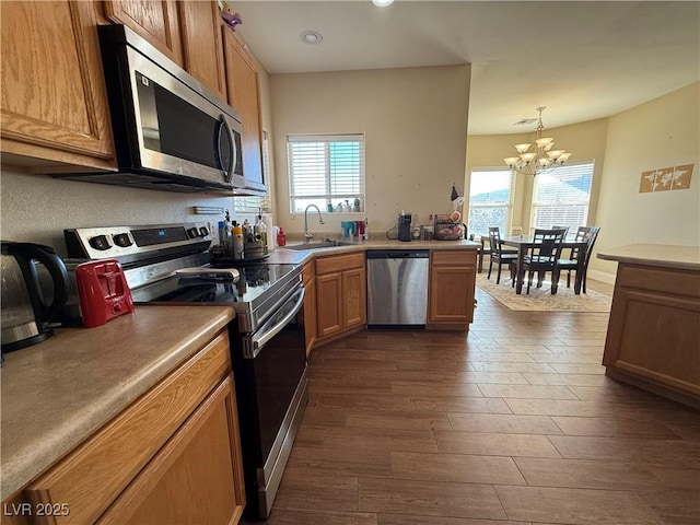 kitchen with appliances with stainless steel finishes, brown cabinetry, a sink, and decorative light fixtures