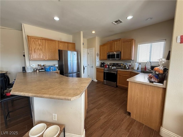 kitchen with visible vents, appliances with stainless steel finishes, a kitchen breakfast bar, dark wood-type flooring, and a peninsula