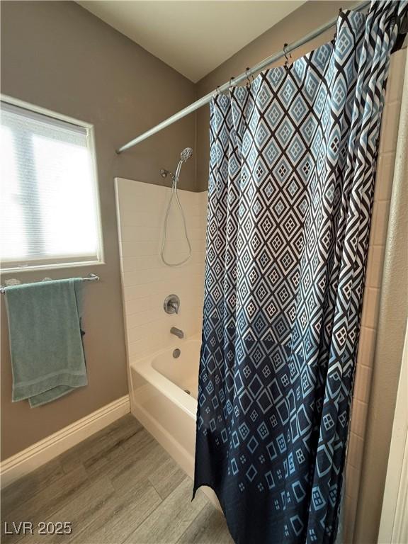 bathroom with wood finished floors, shower / bath combo with shower curtain, and baseboards