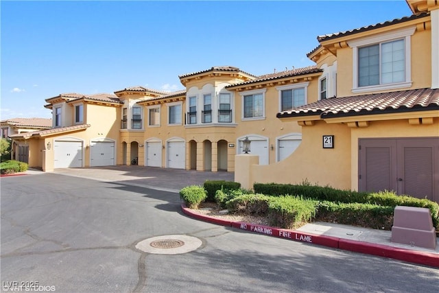 mediterranean / spanish-style home featuring a tiled roof, a garage, driveway, and stucco siding