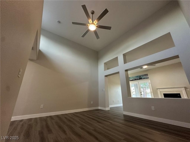 unfurnished living room with a fireplace, dark wood finished floors, a high ceiling, a ceiling fan, and baseboards