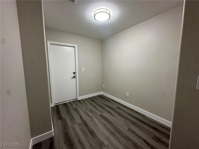 spare room featuring a textured ceiling, dark wood-style flooring, and baseboards