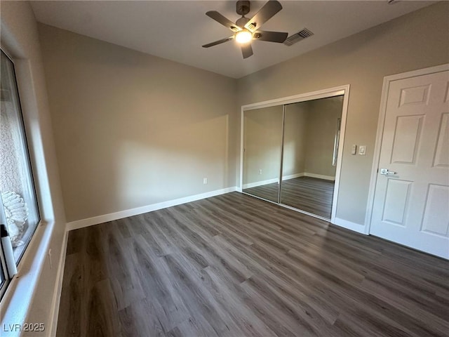 unfurnished bedroom featuring dark wood-style flooring, a closet, visible vents, a ceiling fan, and baseboards