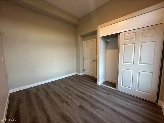 unfurnished bedroom with a closet, baseboards, and dark wood-style flooring