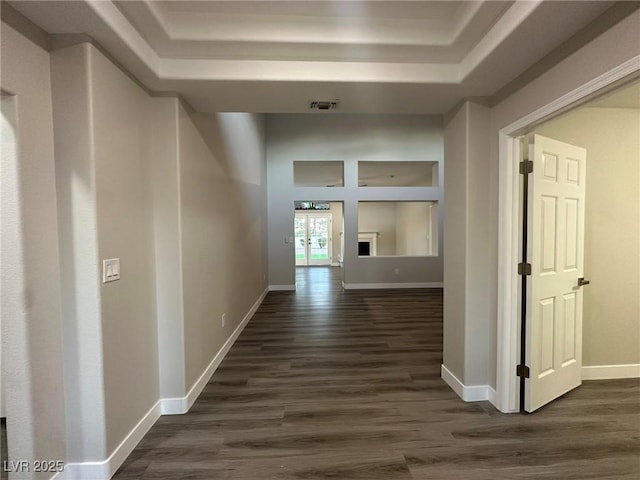 hallway with a tray ceiling, visible vents, dark wood finished floors, and baseboards