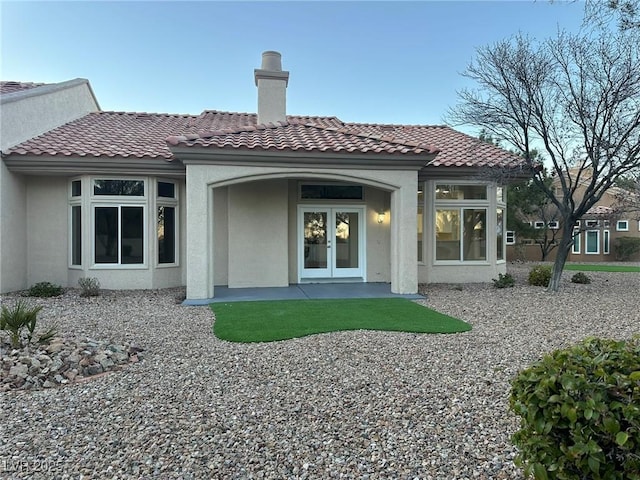 rear view of property featuring a tiled roof, french doors, a chimney, and stucco siding