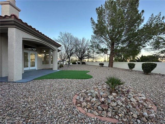 yard at dusk with french doors, a patio area, and a fenced backyard