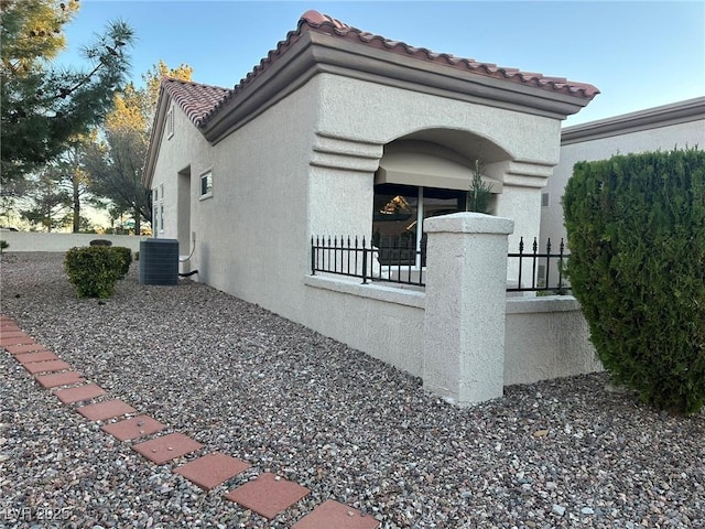 view of home's exterior with a tiled roof, cooling unit, fence, and stucco siding