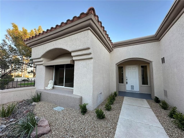 entrance to property with fence, a tiled roof, and stucco siding