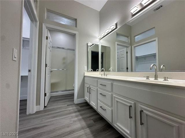 bathroom featuring a sink, wood finished floors, visible vents, a shower stall, and double vanity