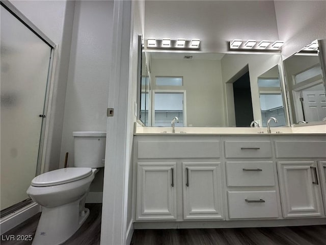 full bathroom with toilet, wood finished floors, a sink, double vanity, and a stall shower