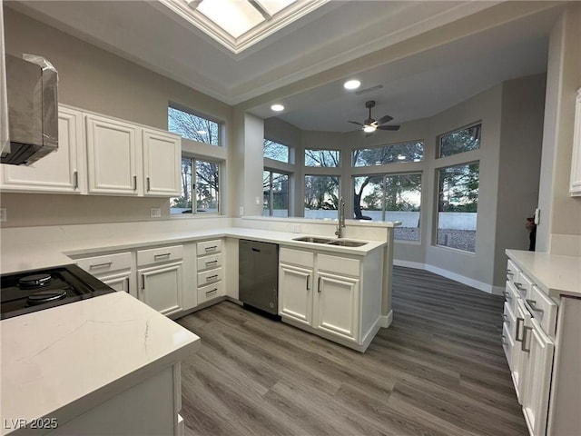 kitchen featuring white cabinets, a sink, wood finished floors, dishwasher, and a peninsula