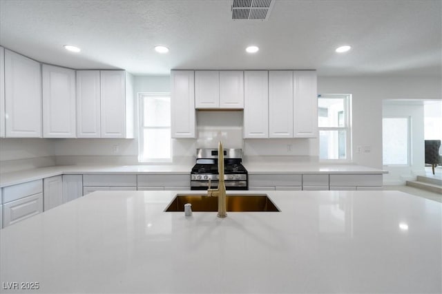 kitchen featuring light countertops, stainless steel gas stove, a sink, and visible vents