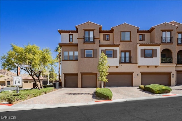 view of front of property featuring decorative driveway, central AC unit, an attached garage, and stucco siding