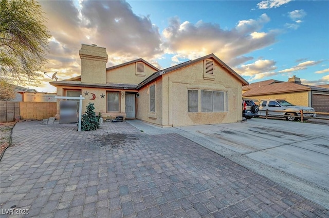 view of front of home with a patio area, a chimney, fence, and stucco siding