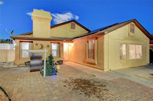 rear view of property with a chimney, a patio area, roof mounted solar panels, and stucco siding