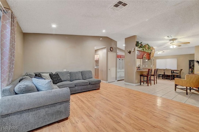 living room featuring lofted ceiling, ceiling fan, visible vents, and wood finished floors