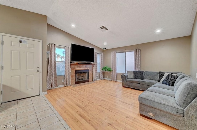 living area with a textured ceiling, a tile fireplace, visible vents, light wood-style floors, and vaulted ceiling