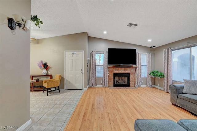 living room featuring a fireplace, visible vents, light wood-style floors, vaulted ceiling, and a textured ceiling