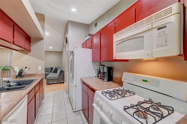 kitchen featuring white appliances, light countertops, red cabinets, and a sink