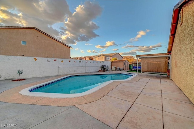 view of swimming pool featuring an outbuilding, a fenced backyard, a fenced in pool, a shed, and a patio area