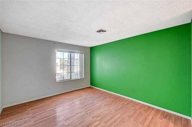 empty room with light wood-type flooring, baseboards, visible vents, and a textured ceiling