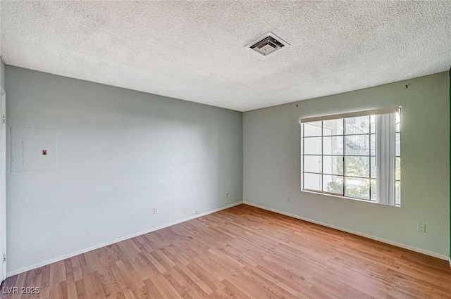 unfurnished room featuring a textured ceiling, light wood-style flooring, visible vents, baseboards, and electric panel