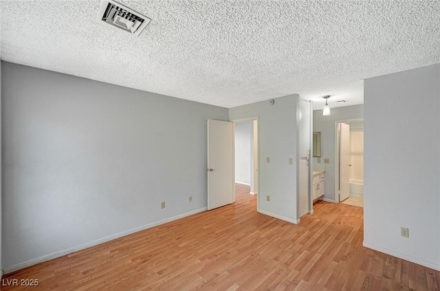 spare room featuring baseboards, visible vents, a textured ceiling, and light wood finished floors