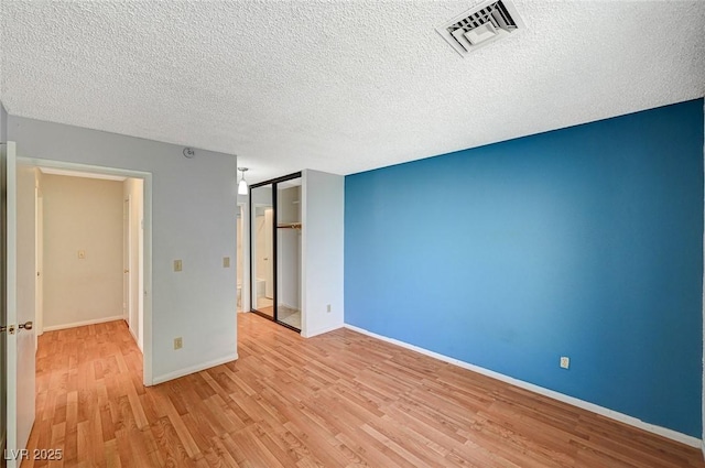 unfurnished room featuring baseboards, a textured ceiling, visible vents, and light wood-style floors