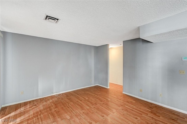 spare room featuring baseboards, a textured ceiling, visible vents, and light wood-style floors