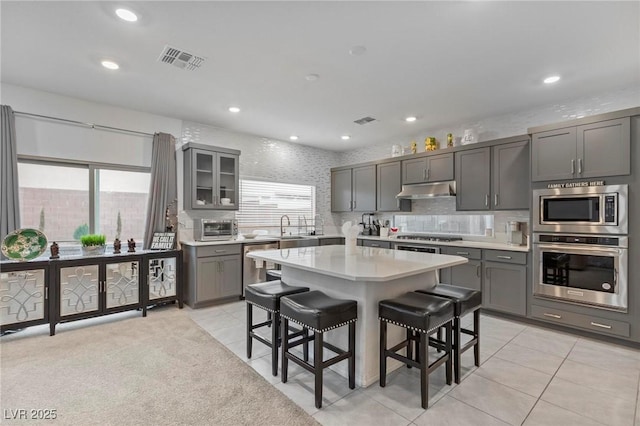 kitchen with a center island, a breakfast bar area, stainless steel appliances, light countertops, and under cabinet range hood