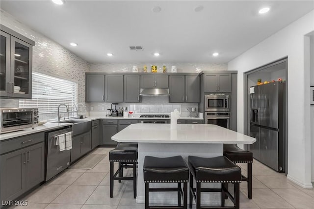 kitchen with visible vents, a kitchen island, stainless steel appliances, light countertops, and under cabinet range hood