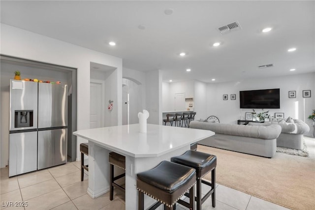 kitchen featuring a breakfast bar area, a kitchen island, visible vents, light countertops, and stainless steel refrigerator with ice dispenser