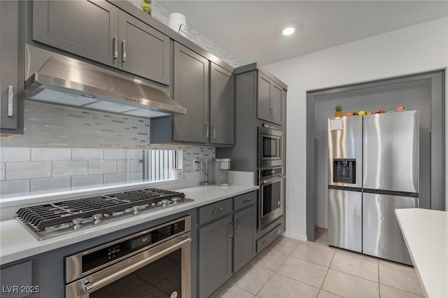 kitchen with light countertops, gray cabinetry, appliances with stainless steel finishes, light tile patterned flooring, and under cabinet range hood