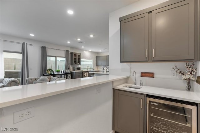 kitchen with wine cooler, gray cabinets, light countertops, a sink, and recessed lighting