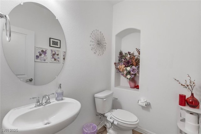 half bath featuring toilet, baseboards, and a sink