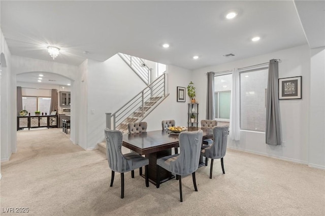 dining room featuring arched walkways, light carpet, recessed lighting, and stairs