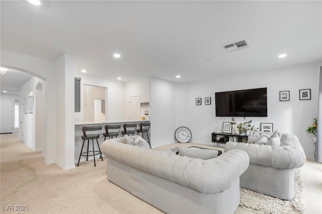 living room with light colored carpet, arched walkways, visible vents, and recessed lighting