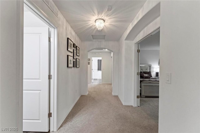 hallway with light carpet, arched walkways, and baseboards