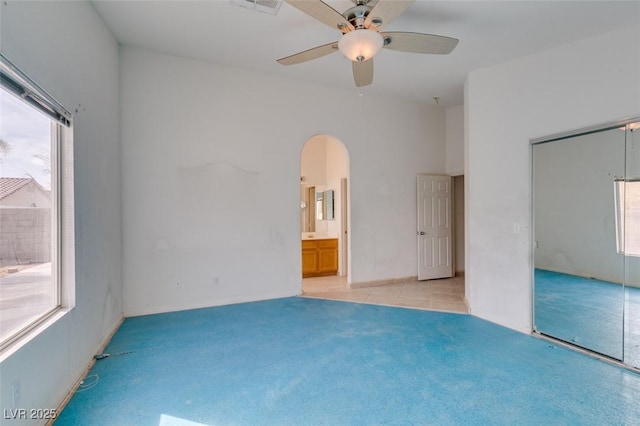 unfurnished bedroom with arched walkways, ceiling fan, light tile patterned floors, light colored carpet, and a closet