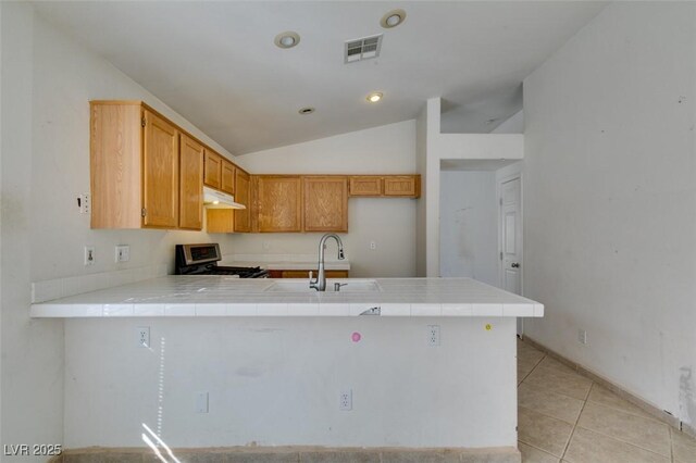 kitchen featuring visible vents, a peninsula, vaulted ceiling, under cabinet range hood, and gas stove