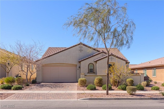 mediterranean / spanish-style house featuring a garage, a tiled roof, decorative driveway, and stucco siding