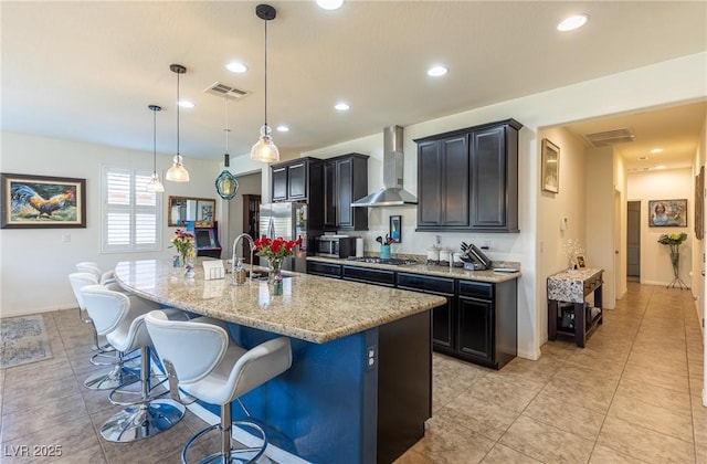 kitchen with an island with sink, wall chimney range hood, visible vents, and stainless steel appliances