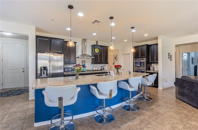 kitchen featuring light stone counters, stainless steel appliances, visible vents, a sink, and wall chimney exhaust hood