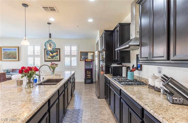 kitchen with light stone counters, pendant lighting, appliances with stainless steel finishes, a sink, and wall chimney exhaust hood