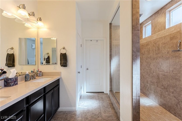 full bath featuring double vanity, tiled shower, a sink, and baseboards