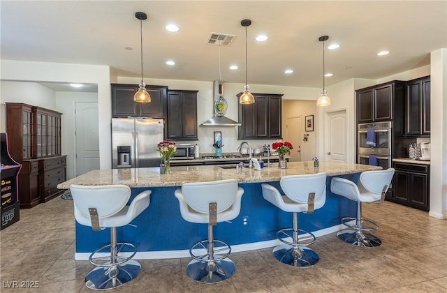 kitchen with light stone counters, a large island, visible vents, appliances with stainless steel finishes, and wall chimney exhaust hood