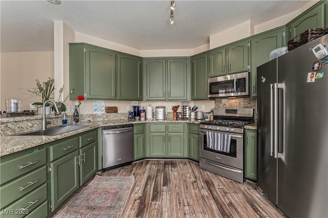 kitchen with light stone counters, dark wood-style flooring, stainless steel appliances, green cabinets, and a sink