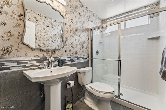 bathroom featuring a wainscoted wall, a textured ceiling, and wallpapered walls